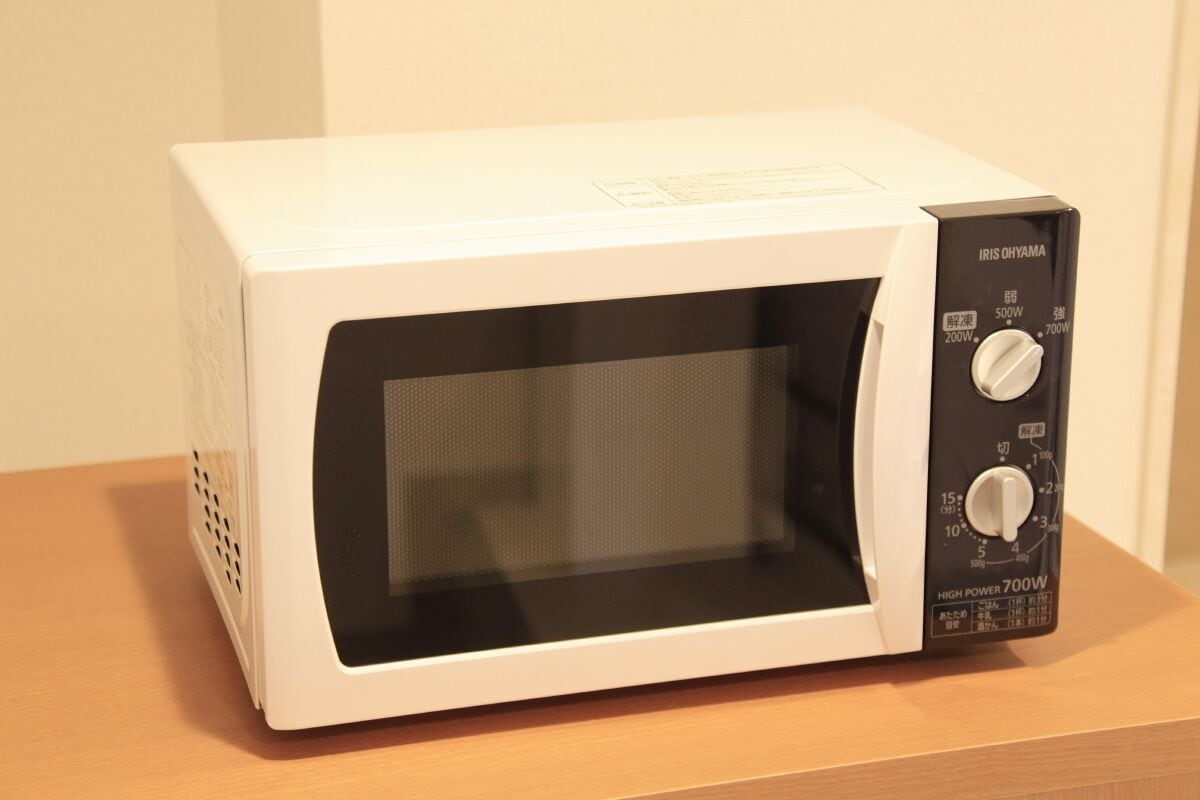 En hvid mikrobølgeovn med sort kontrolpanel og digitalt display, placeret på en træoverflade.
