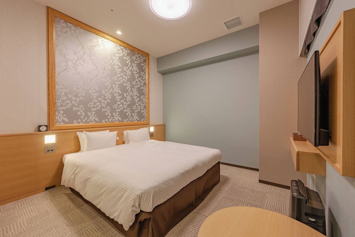 A hotel room with a large bed, a wooden headboard, a wall-mounted TV, and a small desk with a telephone.
