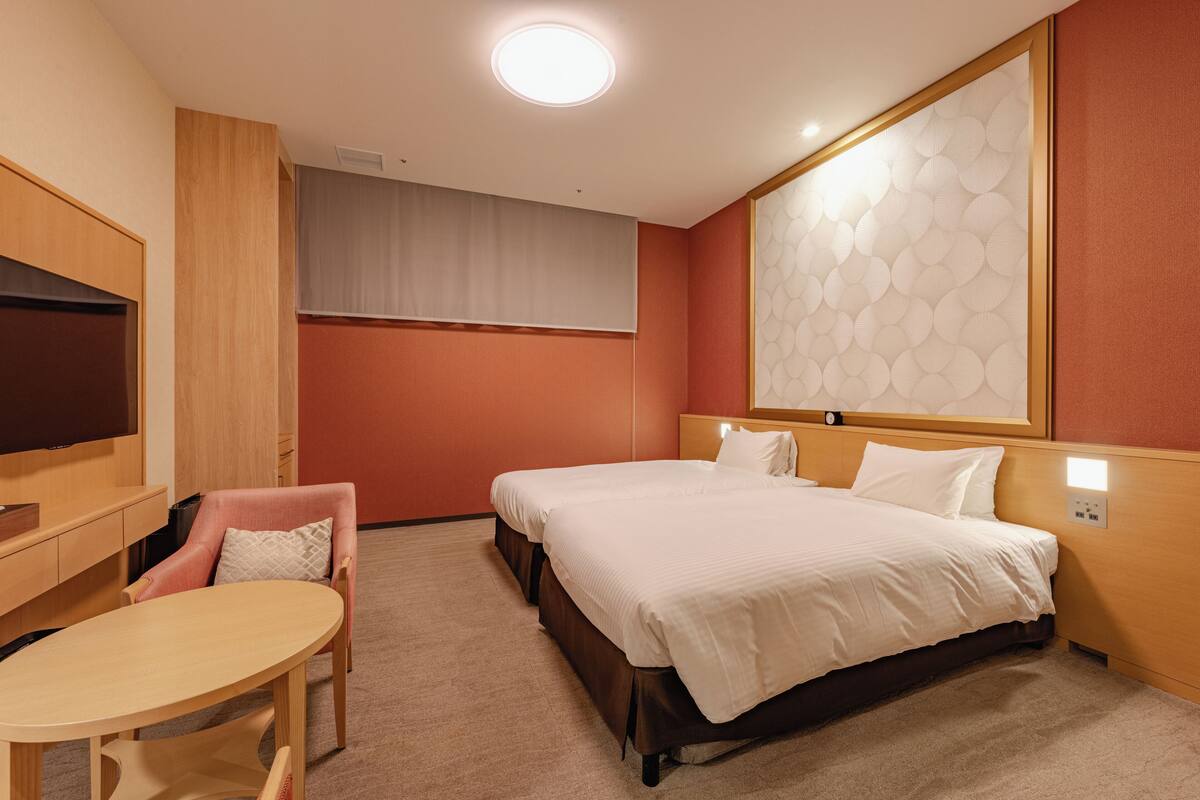 A hotel room with a bed, a desk, a chair, a TV, and a large window.