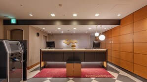 A reception area with a check-in counter, a self-service kiosk, and a red carpet with "Richmond Hotel" text.