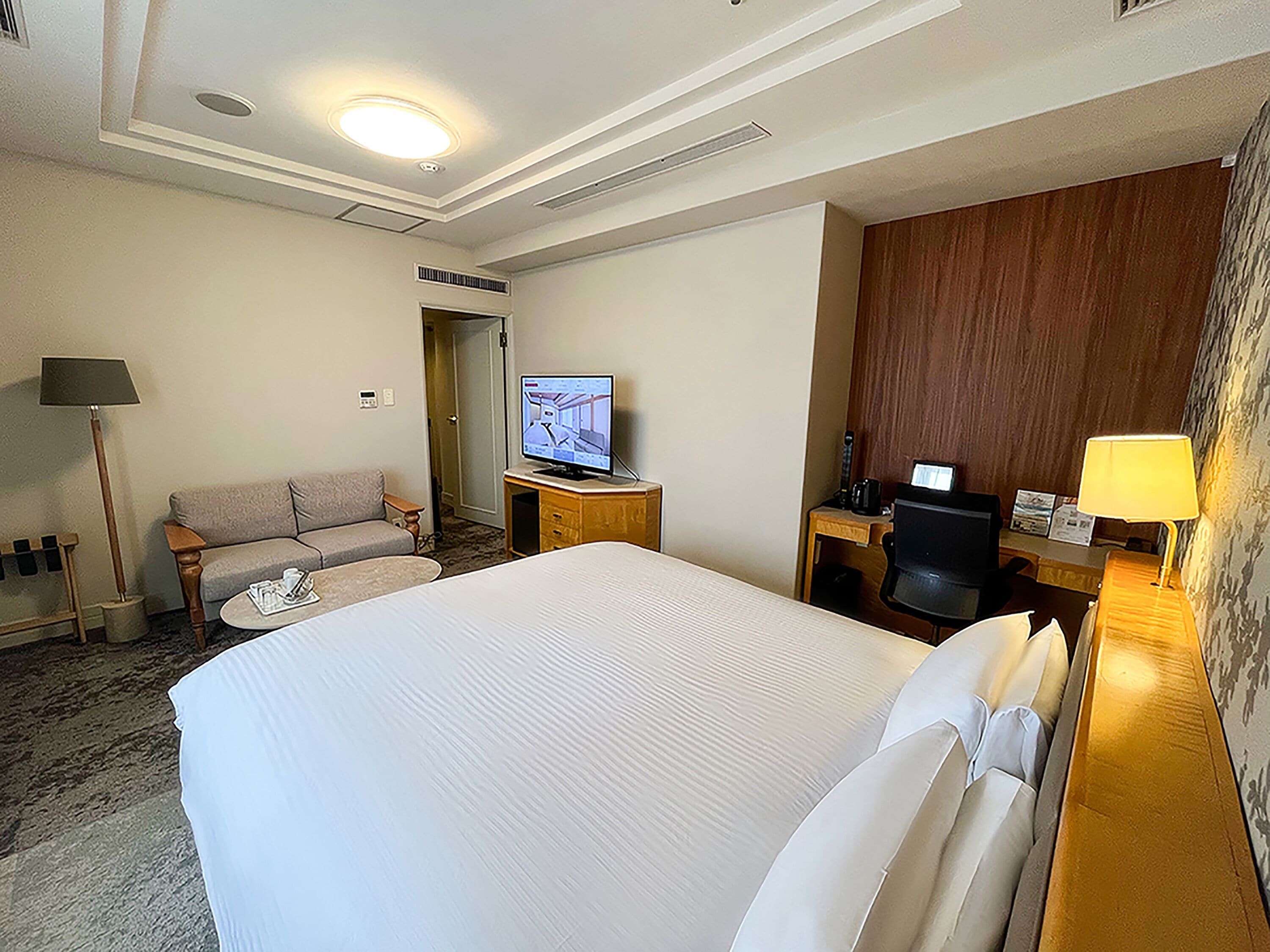Habitación de hotel con una cama grande, televisión, escritorio con silla, sofá y lámpara.