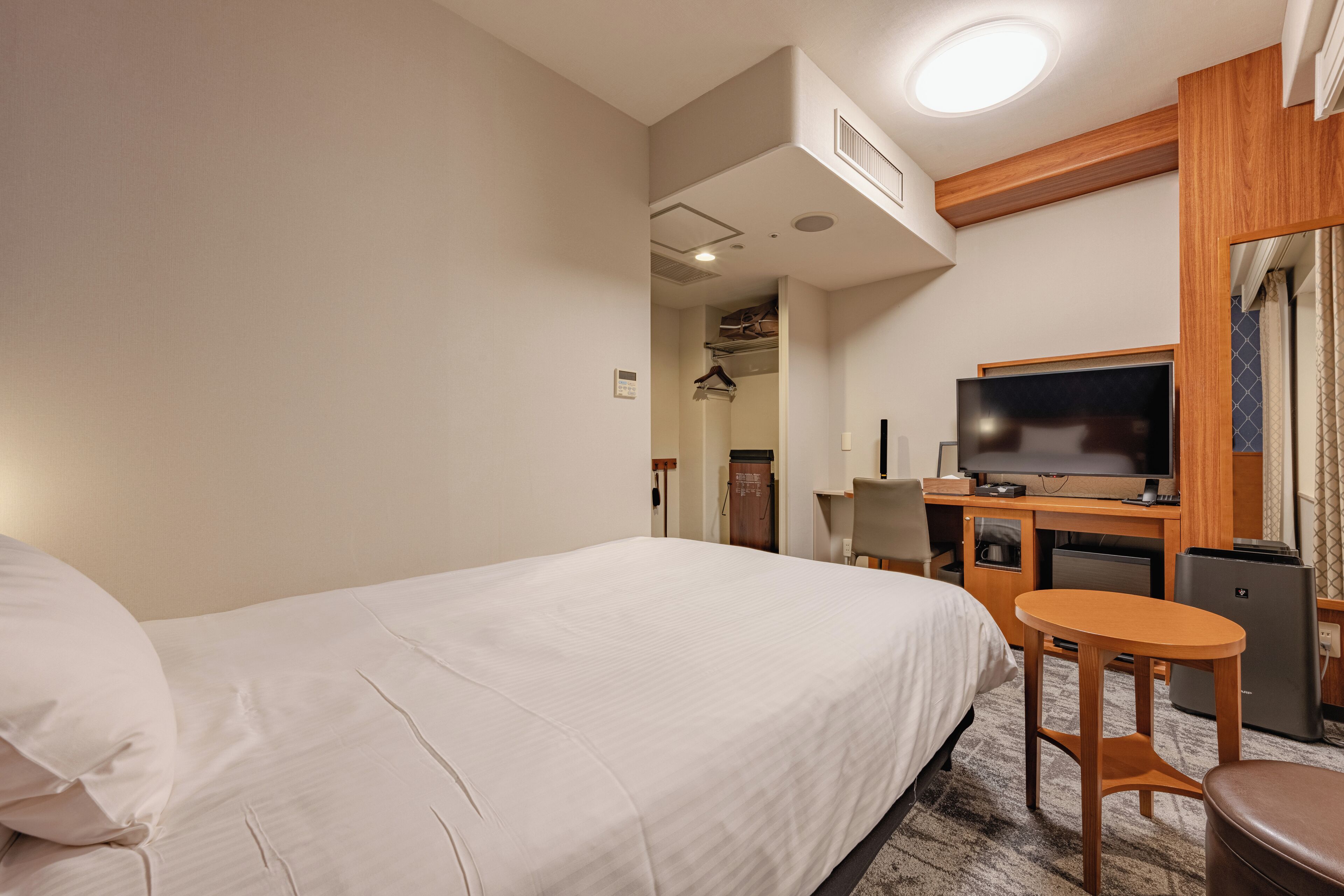 A hotel room with a bed, a desk, a television, and a small table.