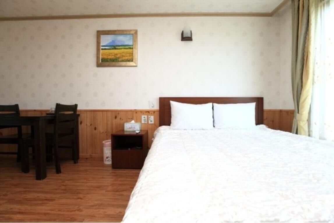 A hotel room with a wooden floor, a bed with white bedding, a nightstand, a chair, a small table, and a painting on the wall.