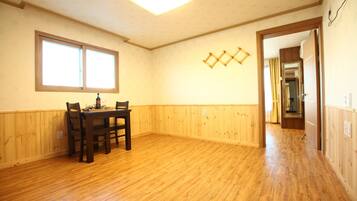 Una habitación con suelo de madera, una mesa de comedor con sillas, una ventana y una puerta que da a otra habitación.