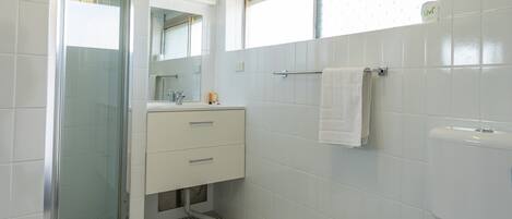 Et badeværelse med bruser, håndvask og toilet.