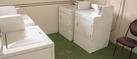 A laundry room with stacked washers and dryers, a chair, and a utility wall with electrical outlets.