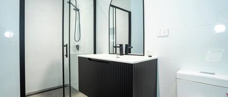 Un baño moderno con ducha de vidrio, tocador con espejo y retrete.