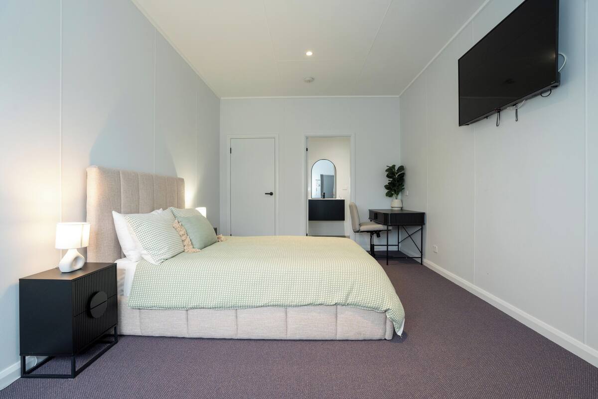 A bedroom with a bed, bedside table, TV, and a desk with a chair.