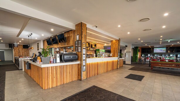 Una zona de recepción con mostrador de madera, mesa de billar y área de bar con varias pantallas.