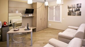 A modern living room with a sofa, a dining table with chairs, a TV, and a wooden cabinet. - Marbia Guest House (Bologna)