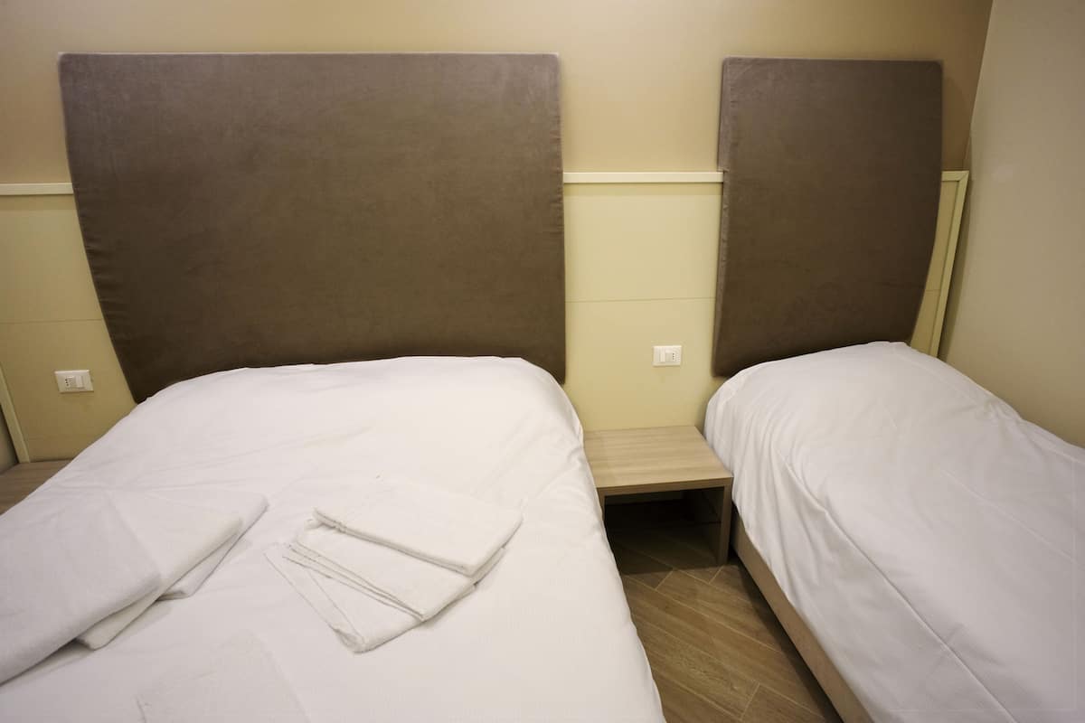 Dos camas individuales con cabeceras marrones, ropa de cama blanca y una mesita entre ellas.