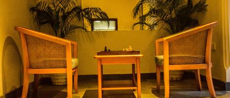 Una habitación con dos sillas de madera y una mesita pequeña, rodeada de plantas en macetas.