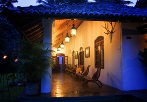 An outdoor covered patio with wooden chairs and tables, a wall-mounted deer head, and hanging lanterns. - Athulya Villas (Udunuwara)