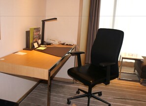 Habitación de hotel con un escritorio de madera, una silla de oficina negra, un teléfono y una lámpara.