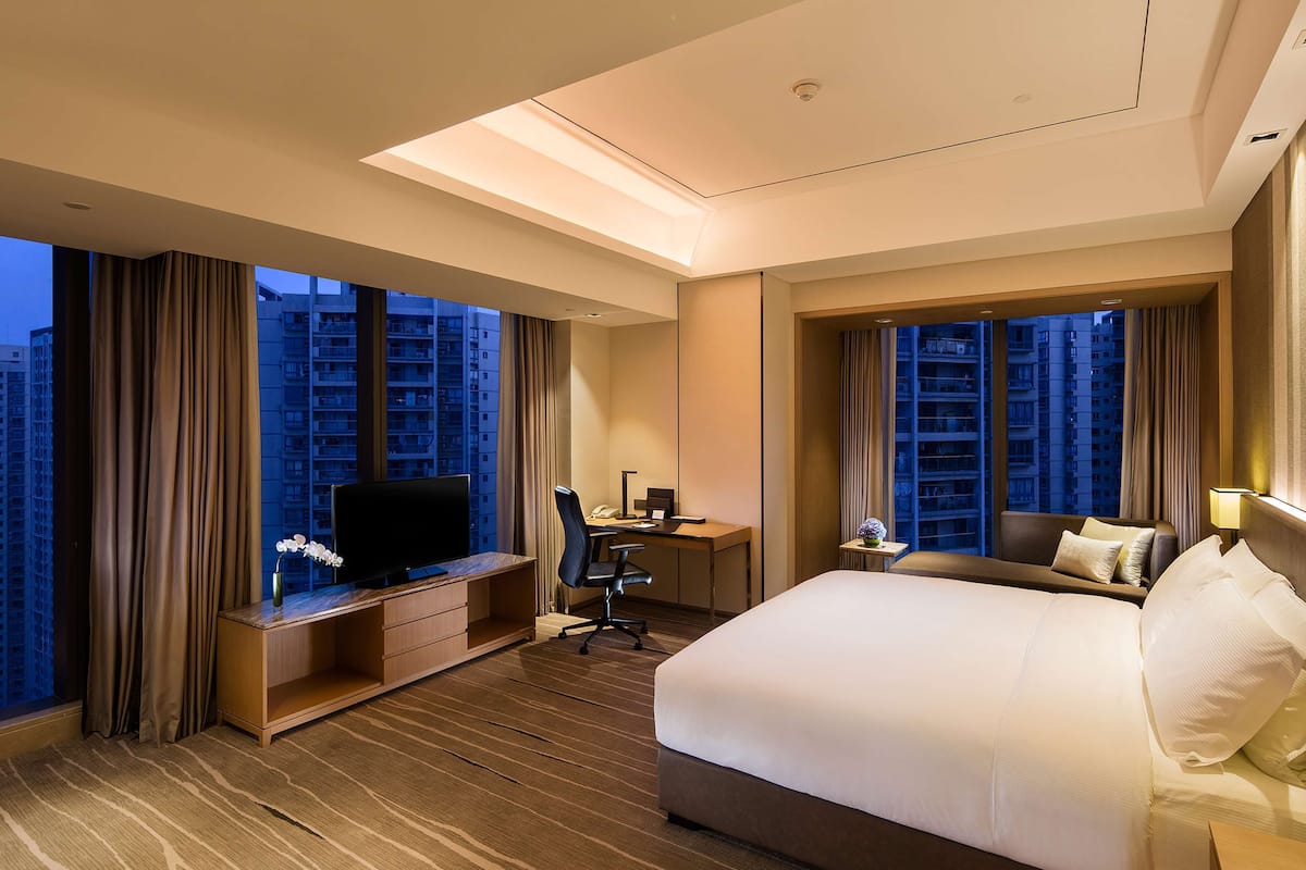Une chambre d’hôtel avec un grand lit, un bureau avec une chaise, une télévision et une vue sur les gratte-ciel.