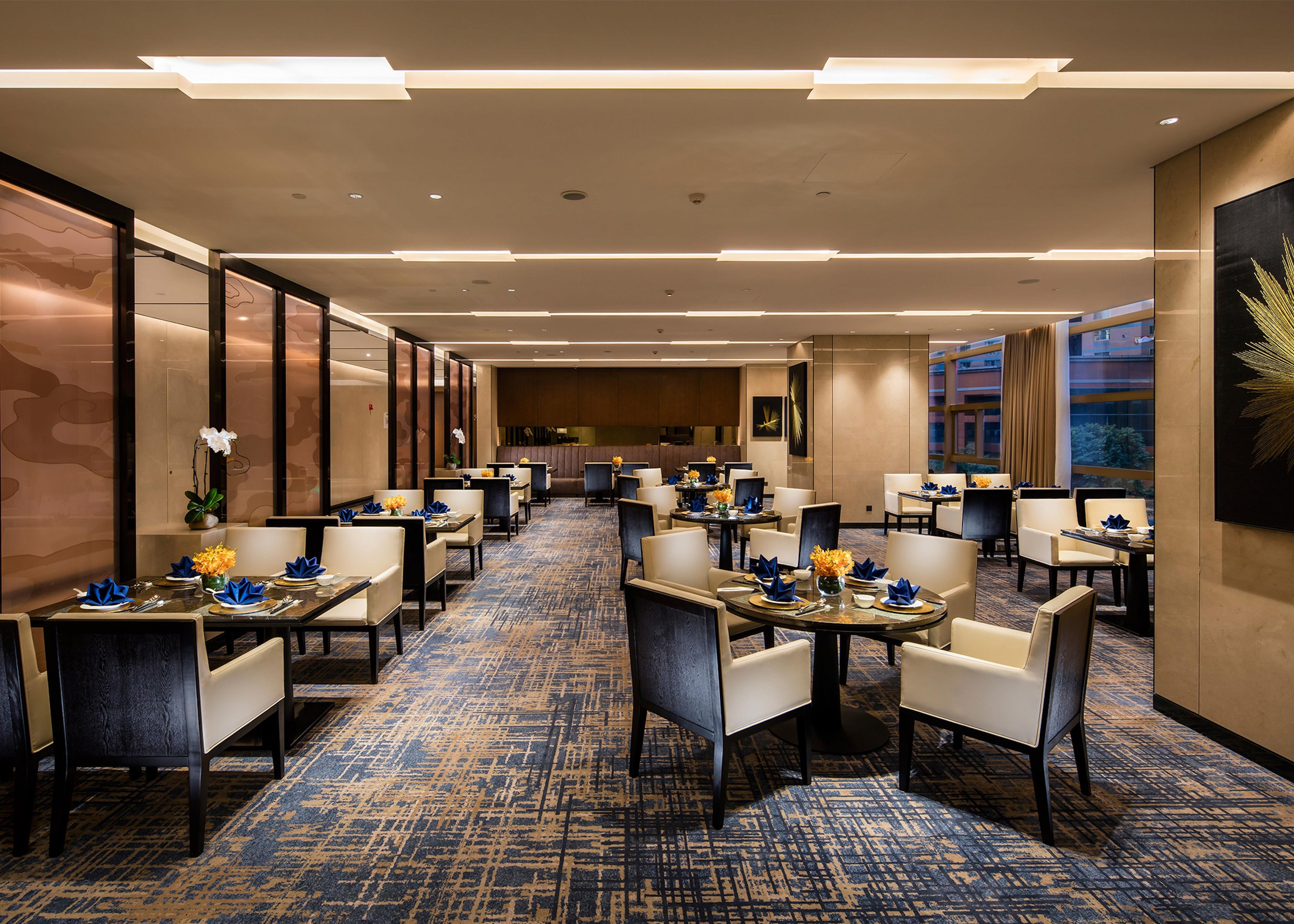 A hotel lobby with multiple dining tables, chairs, and a carpeted floor.