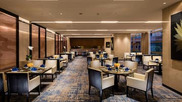 A hotel lobby with multiple dining tables, chairs, and a carpeted floor.