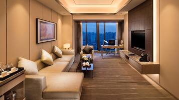 A modern hotel room with a sofa, a desk, a television, and a city view.