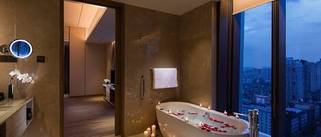 Ein modernes Badezimmer mit einer freistehenden Badewanne, einem Waschtisch mit Spiegel und Blick auf die Stadt durch große Fenster.