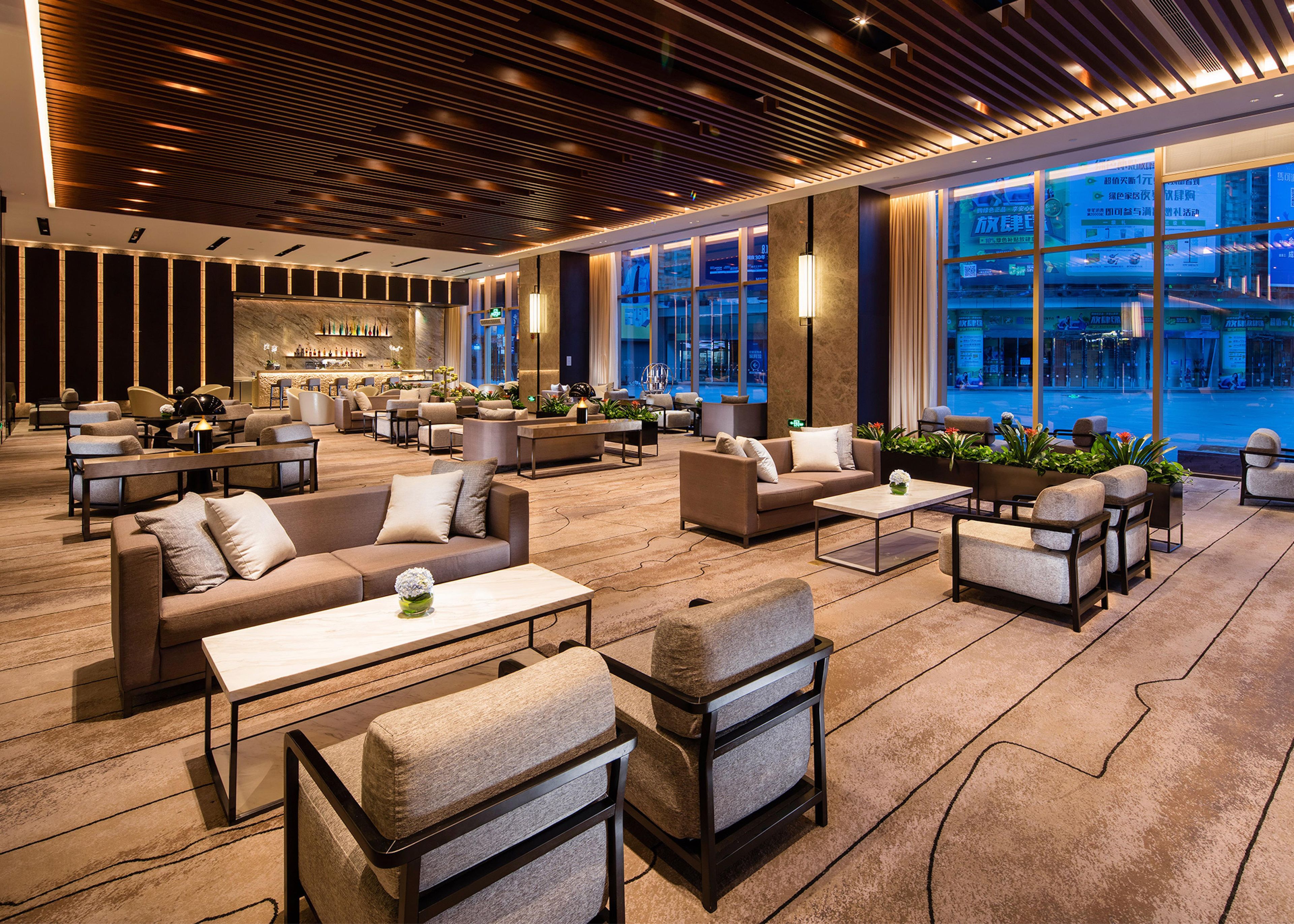 A spacious lobby with multiple seating areas, a bar, and large windows offering a view of the city.
