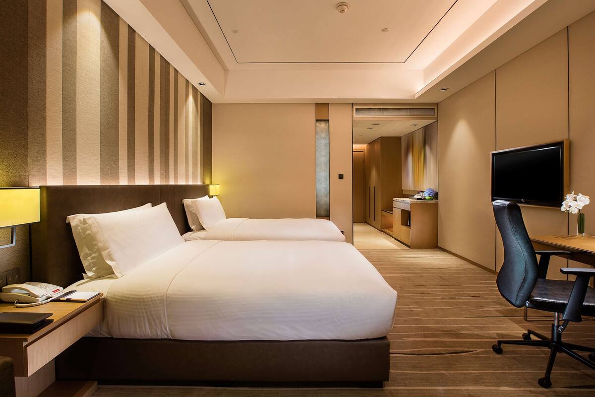 Une chambre d’hôtel avec deux lits, un bureau avec un téléphone, une télévision et une petite kitchenette.