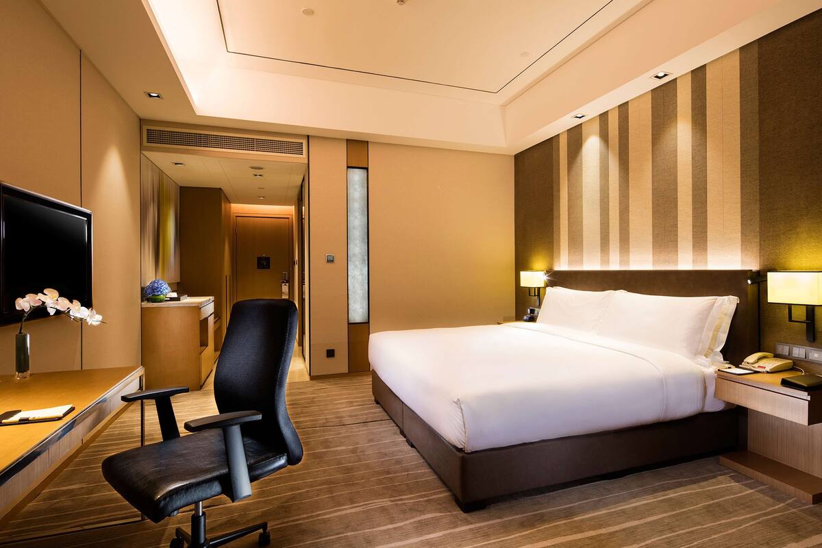 Une chambre d’hôtel équipée d’un lit, d’un bureau, d’une chaise, d’une télévision et d’un téléphone fixé au mur.