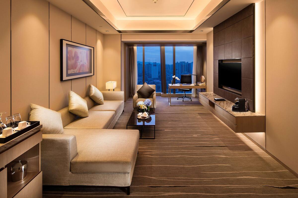 Une chambre d’hôtel moderne équipée d’un canapé, d’un bureau, d’une télévision et offrant une vue sur le paysage urbain.