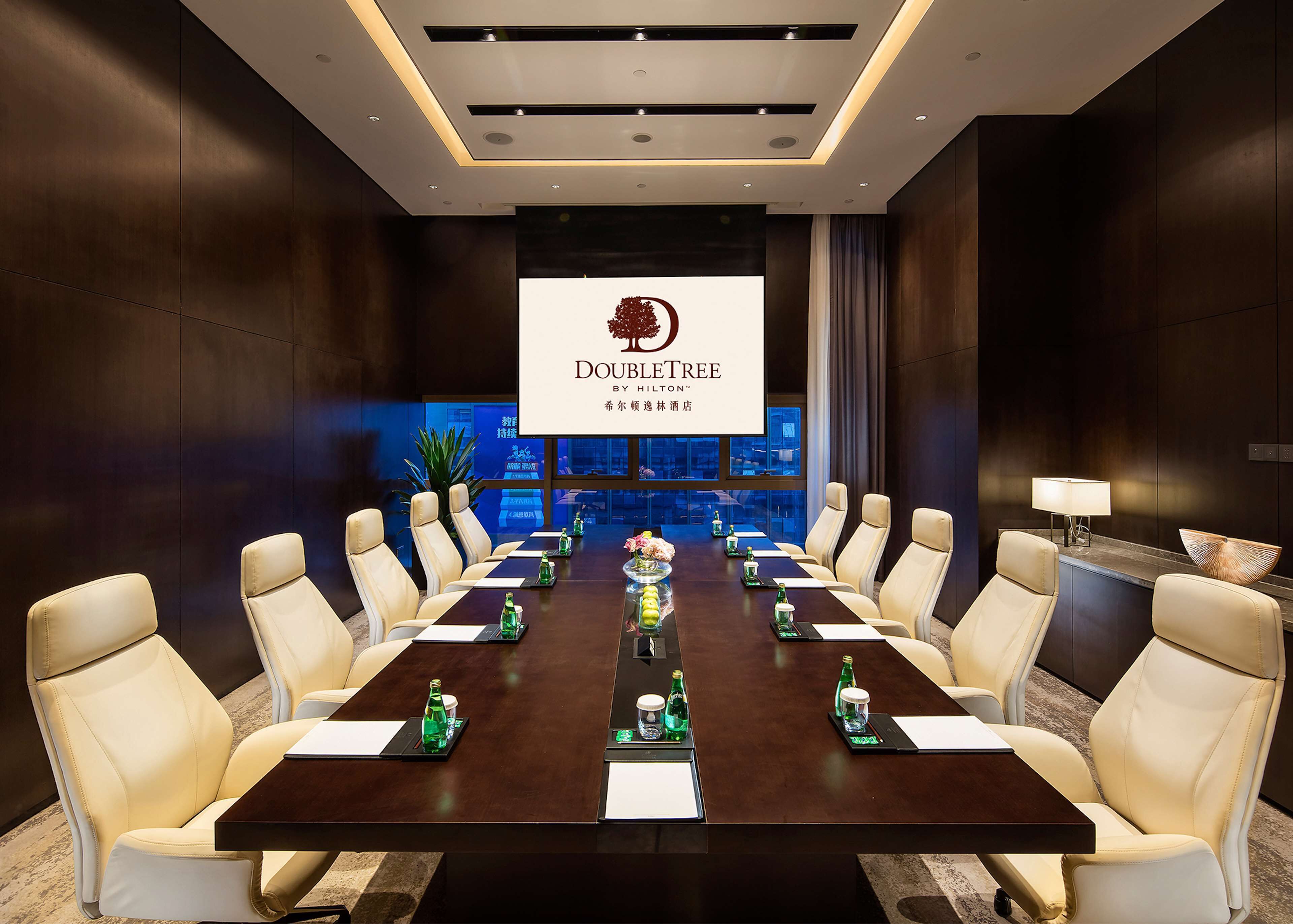 Een vergaderzaal met een lange tafel, meerdere stoelen en een groot scherm waarop het DoubleTree-logo staat.