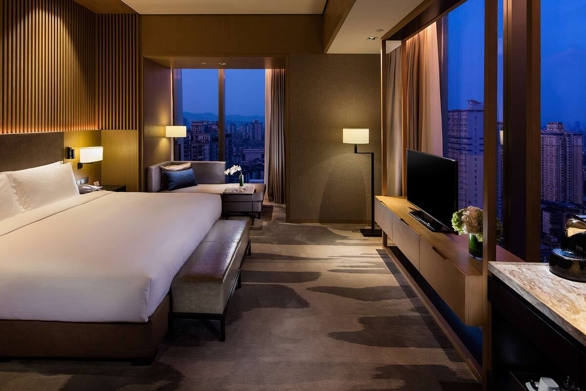 Une chambre d’hôtel avec un grand lit, un bureau avec une télévision, une vue sur la ville et un panorama urbain visible par la fenêtre.