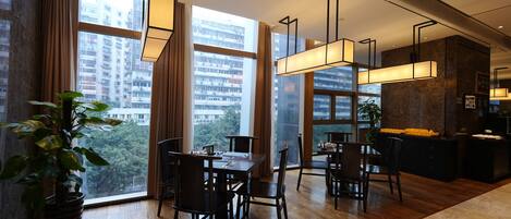 A modern dining area with a large window, wooden flooring, and contemporary lighting fixtures.