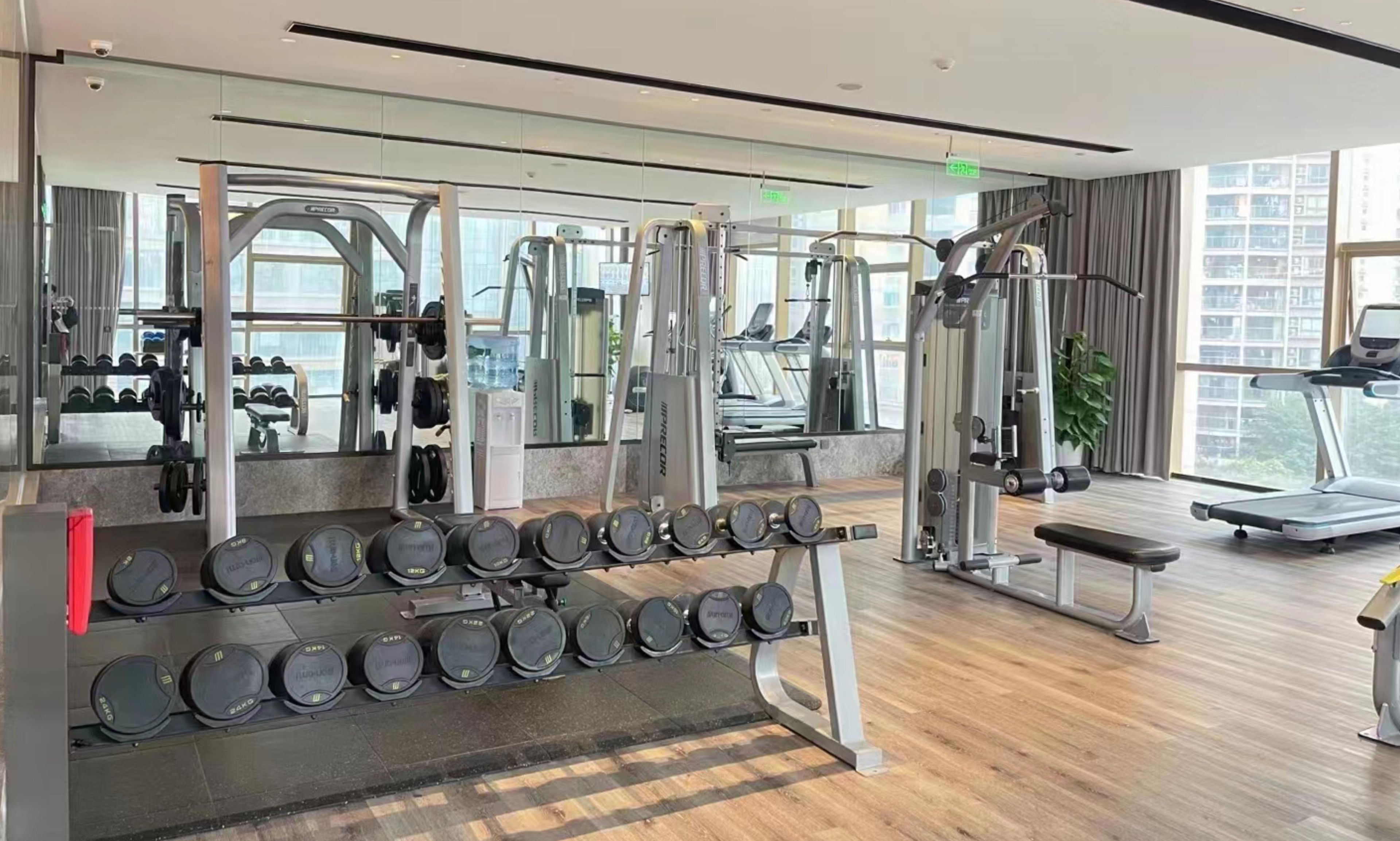 Un gimnasio con equipo de levantamiento de pesas, cintas de correr y una banca.