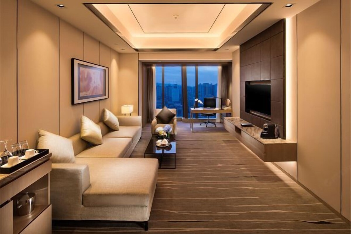 Una habitación de hotel moderna con sofá, zona de comedor, televisión y vistas a la ciudad.