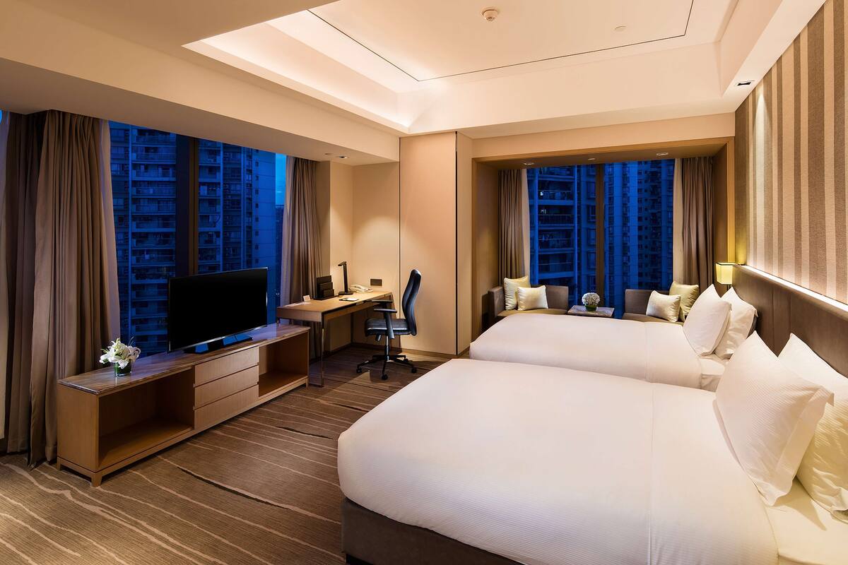 Une chambre d’hôtel avec un grand lit, un bureau avec un ordinateur, une télévision et une vue sur le paysage urbain.