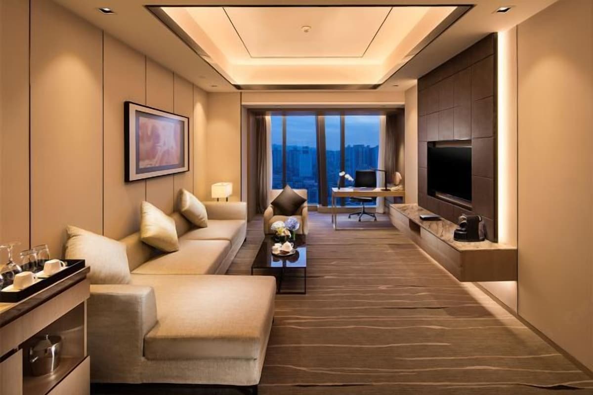 Quarto de hotel moderno com sofá, área de jantar, televisão e vista para a cidade.