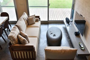 A modern living room with a sofa, a round ottoman, and a flat-screen TV.