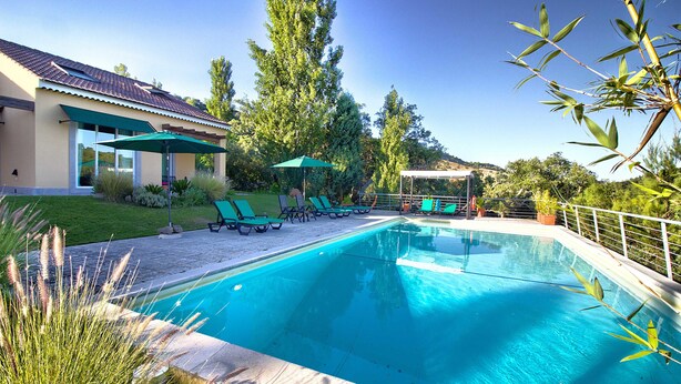 A swimming pool with lounge chairs and umbrellas, surrounded by greenery and a house. - Halma - Nature & Sea (Palmela)