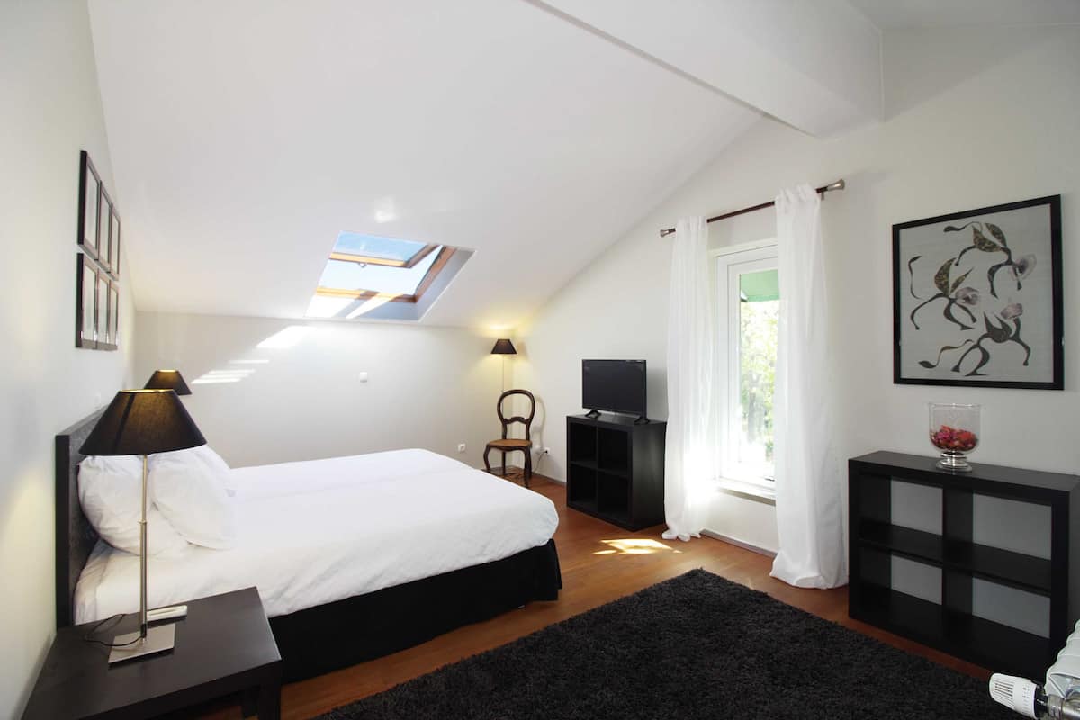 Un dormitorio con cama, escritorio, televisión, silla y ventana con cortinas.