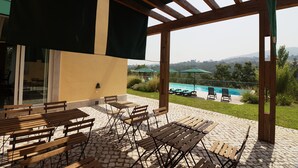 An outdoor patio with wooden tables and chairs, a pool, and a view of the landscape. - Halma - Nature & Sea (Palmela)