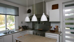 A modern kitchen with a central island, stainless steel appliances, and pendant lighting. - Halma - Nature & Sea (Palmela)