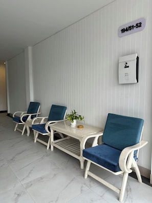 A row of white chairs with blue cushions, a small table with a plant, and a mail box on a white wall. - HOUSE HOTEL Walking Street Pattaya (Pattaya)
