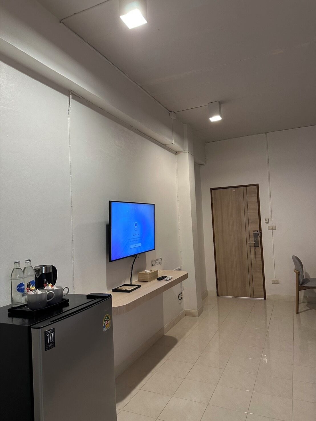 Ein Hotelzimmer mit Flachbildfernseher, Minibar, Holztür und einem Sessel.
