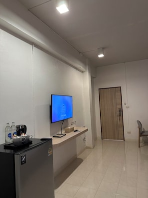 A hotel room with a flat-screen TV, a minibar, a wooden door, and a chair. - HOUSE HOTEL Walking Street Pattaya (Pattaya)