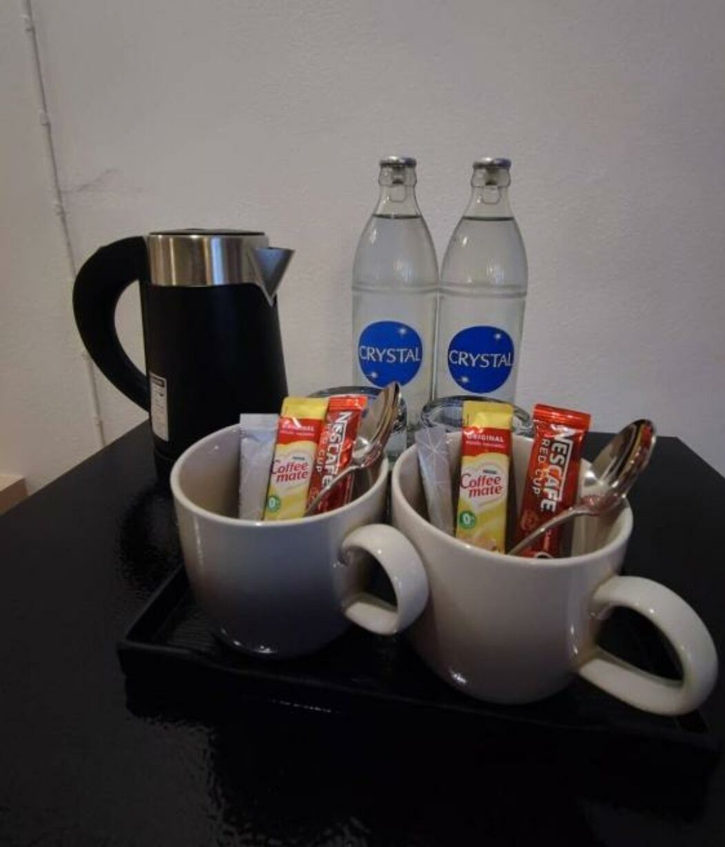 A coffee station with two white mugs, two Crystal water bottles, a black coffee pot, and packets of Nescafé Red Cup coffee.