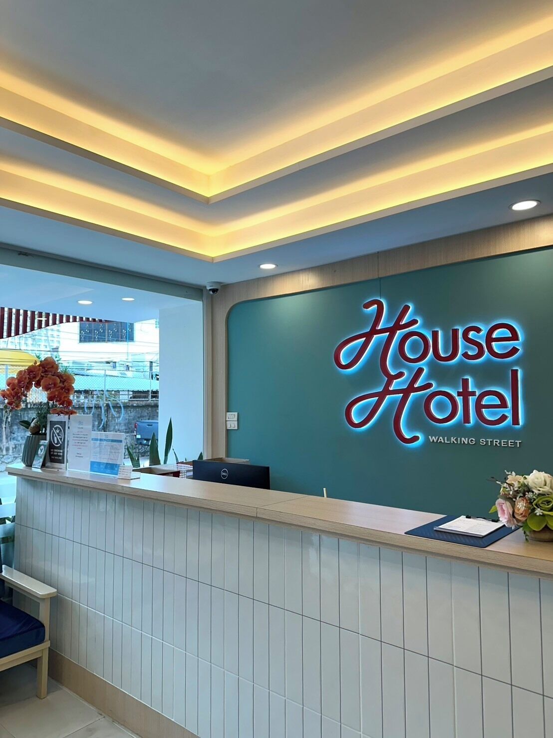A hotel reception desk with a neon sign reading 'House Hotel' and a view of the outside.