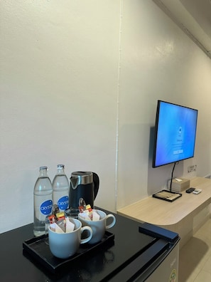 A hotel reception desk with a TV screen, a coffee machine, and a tray with cups and bottled water. - HOUSE HOTEL Walking Street Pattaya (Pattaya)