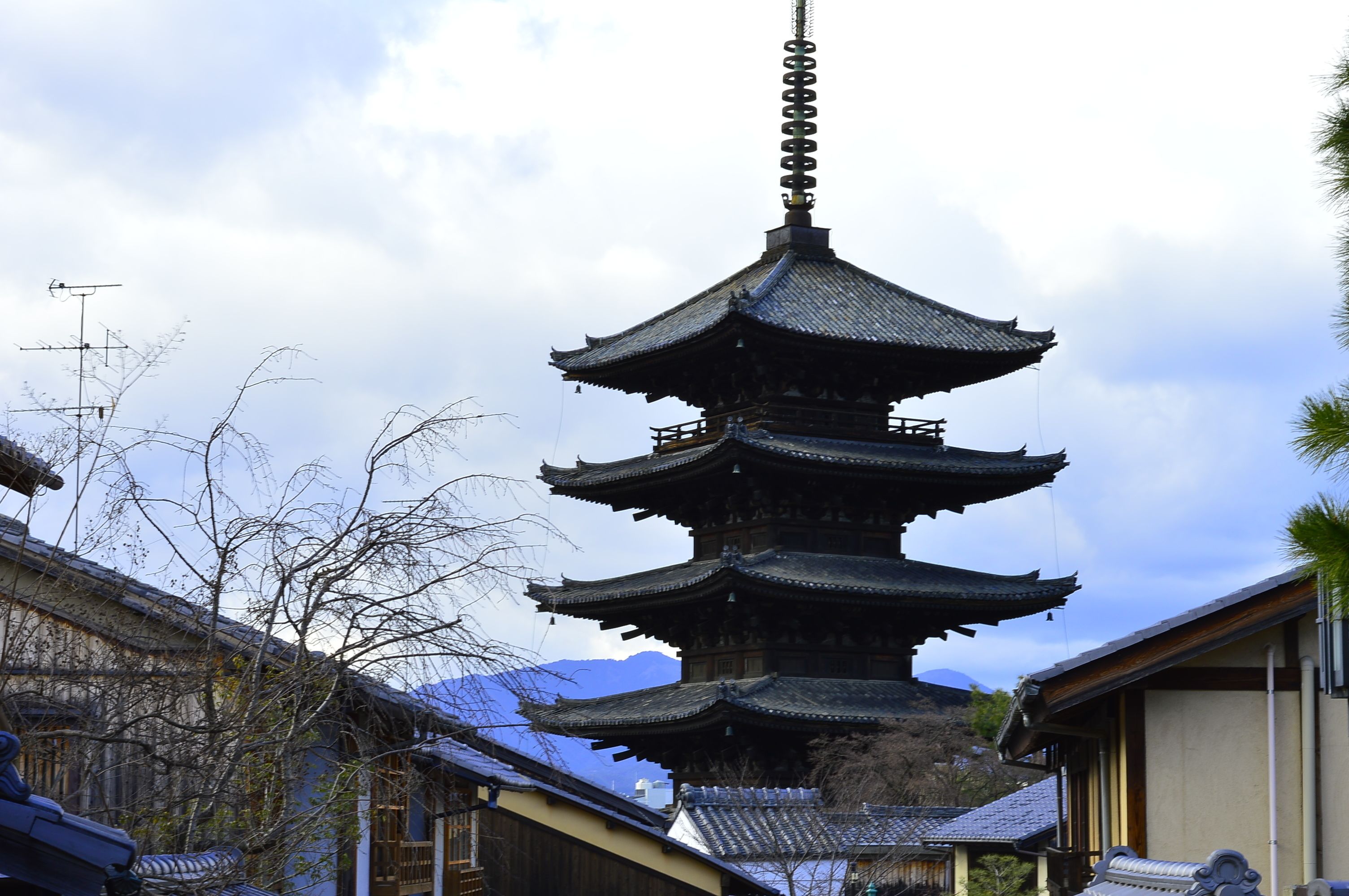 Una pagoda tradicional de varios niveles, con un techo empinado y alicatado, rodeada de edificios con fachadas de madera y techos de tejas.