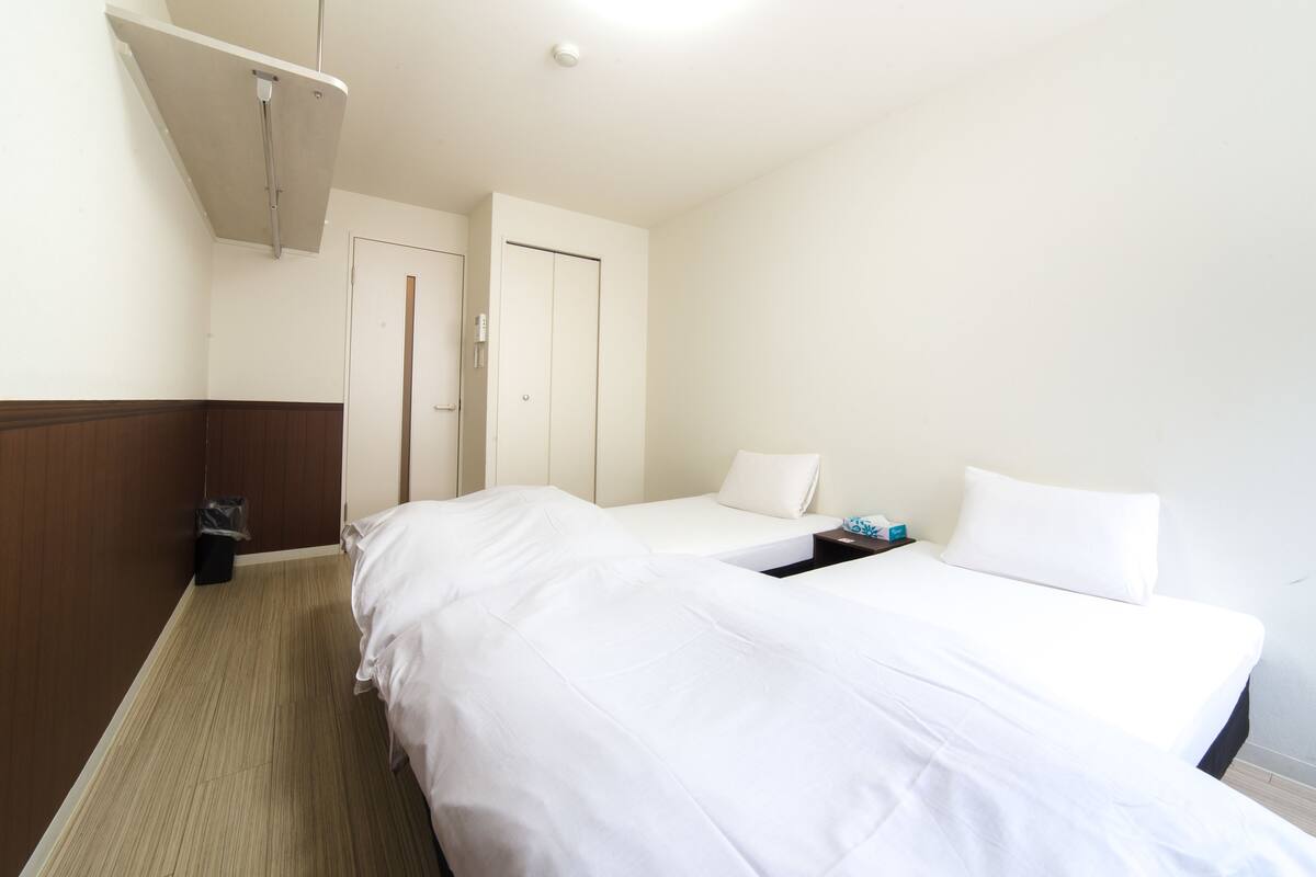 Een hotelkamer met twee bedden, een houten vloer, een prullenbak en een plafondlamp.