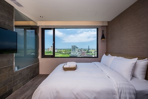 A modern hotel room with a large bed, a flat-screen TV, and a view of the cityscape through large windows. - Angels Inn Jiaoxi Hotspring (Jiaoxi)