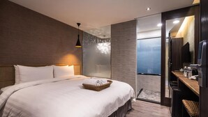 Une chambre d’hôtel moderne avec un grand lit, une tête de lit en bois, une table de chevet avec une lampe et une vue sur la mer par une porte vitrée.