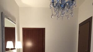 A room with a wooden door, a white desk with a lamp, a chair, and a chandelier. - Domus Mea- Adults Only (Verona)